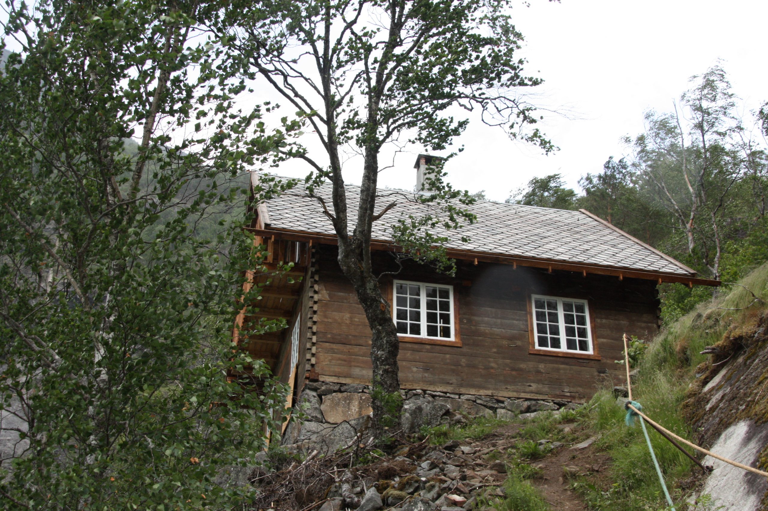 Wittgensteins hus sett nedanfrå i landskapet. Huset står på ei hylle i fjordlandskapet omslutta av fjell og trær.