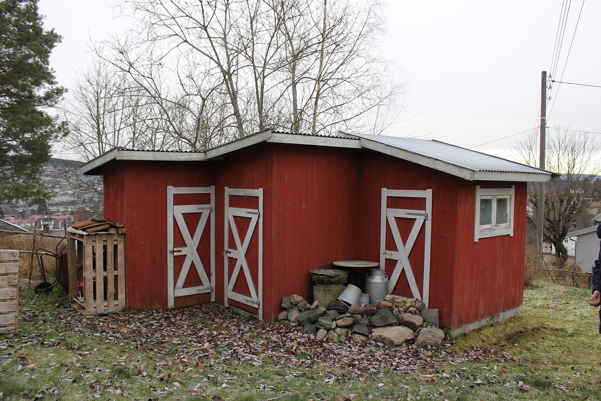 Bildet viser uthuset, et lite rødt trehus med tre små dører i låvestil, med hvite detaljer.