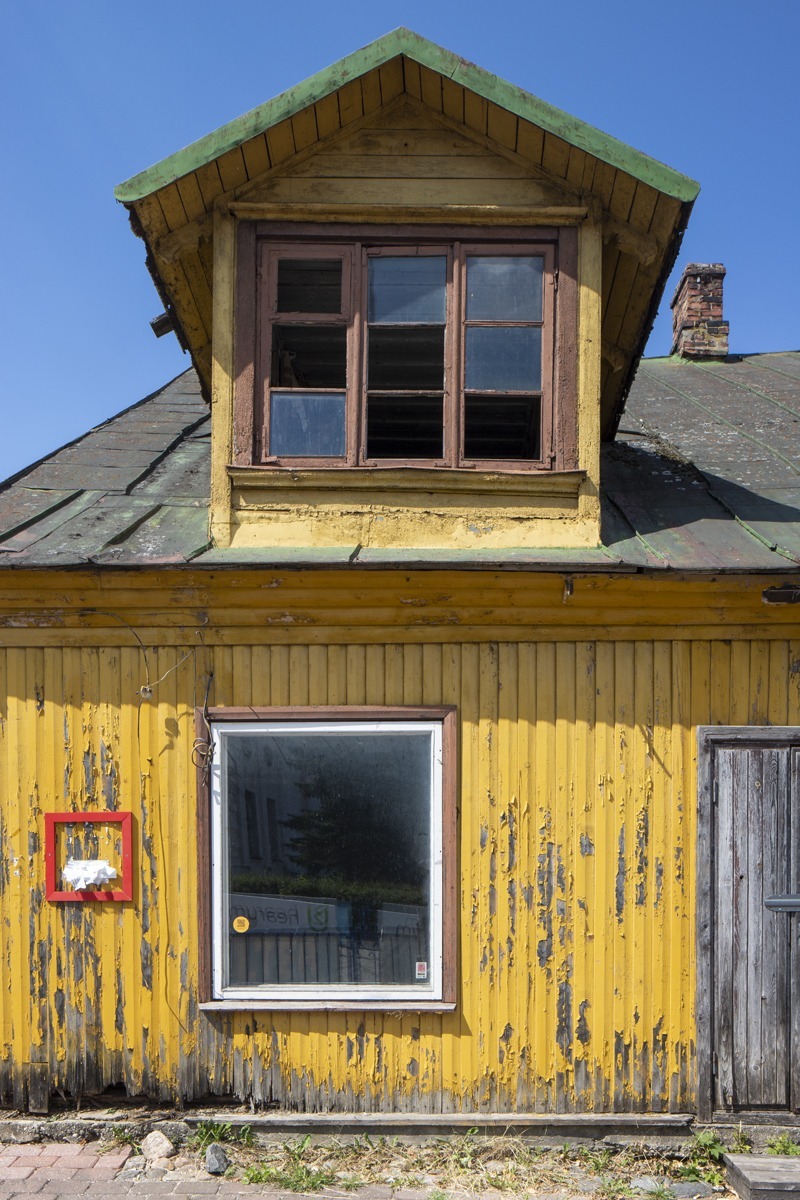 Nærbilde av en to-etasjers bygning med gul maling som flasser av og med delvis intakte vinduer.