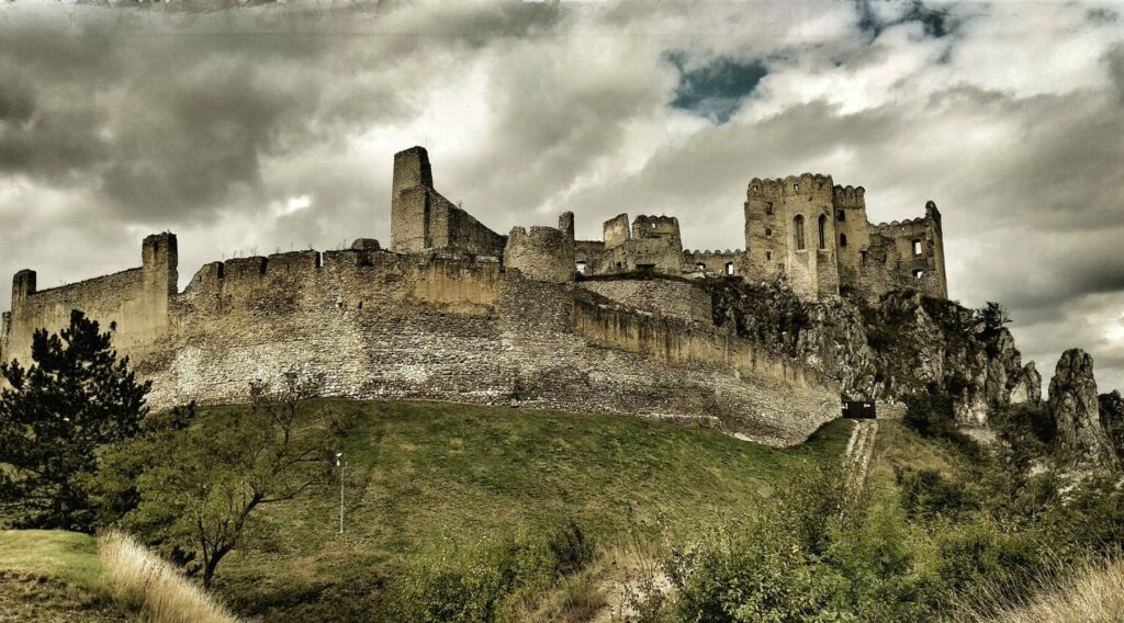 Ruiner av et slott oppe på en klippe med mur og trær.