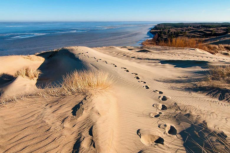 Sanddyner, strå og langstrakt strand, bølger som slår opp mot stranden.