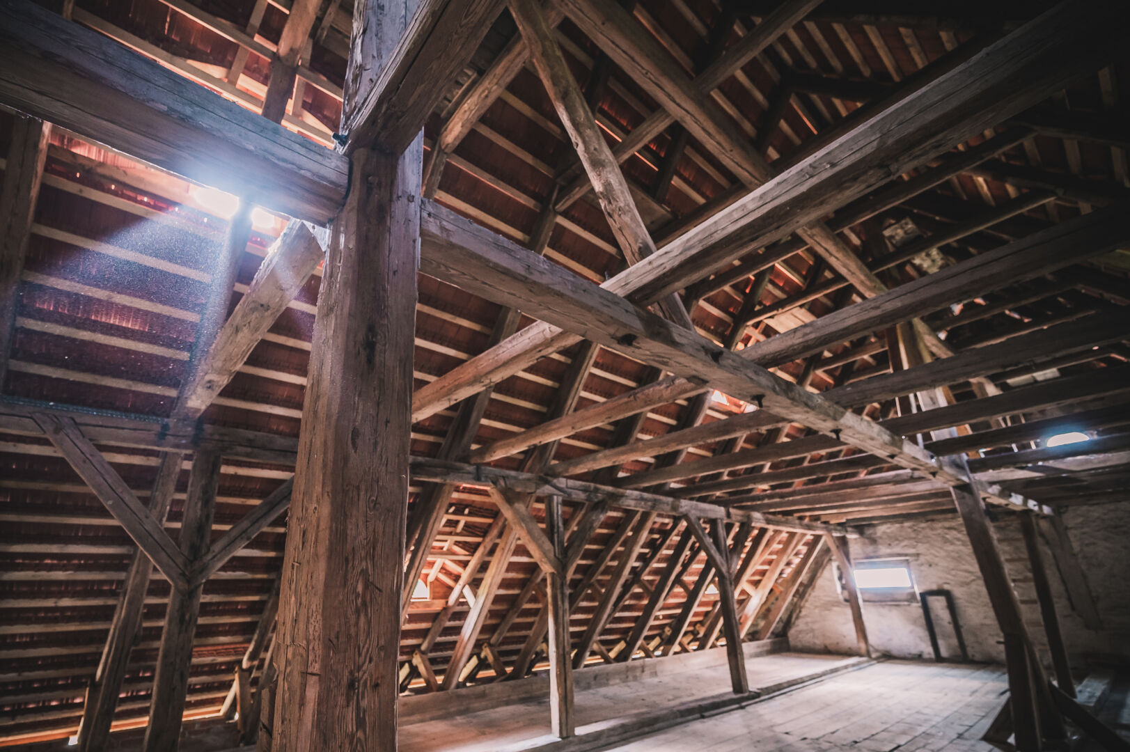 Innvendig på loftet av et tidligere kornmagasin, med lys som skinner gjennom en omfattende trekontruksjon av påler og trebjelker.
