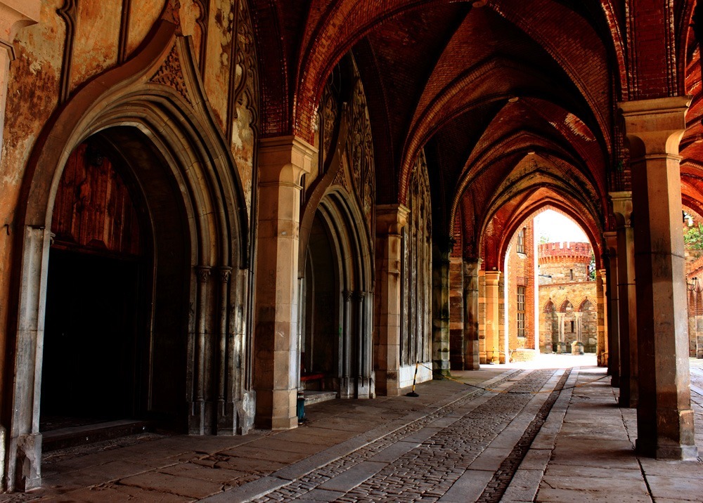 Svalgang i et gotisk palass i rød murstien, dekorert steingulv og søyler på rekke.
