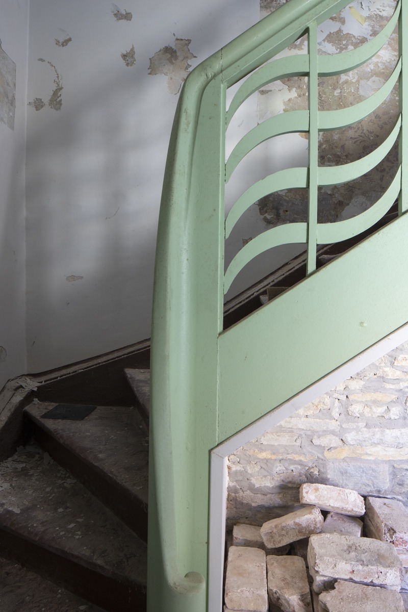 Detaljbilde av en trapperekkverk som er dekorert og malt i lysegrønt, i en forfallen murbygning.